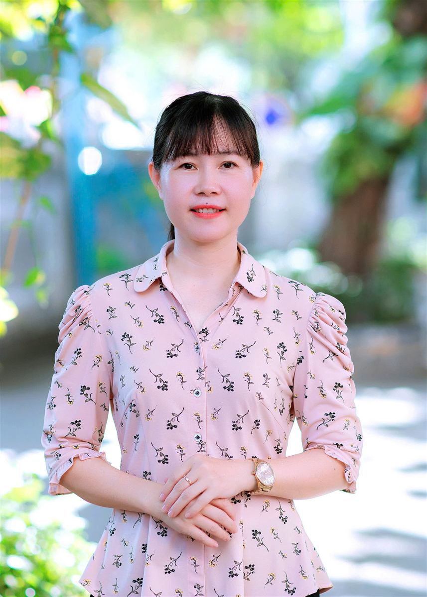 Cô Võ Thị Minh Yến mặc áo hoa hồng nhạt, đứng chắp tay, mỉm cười
